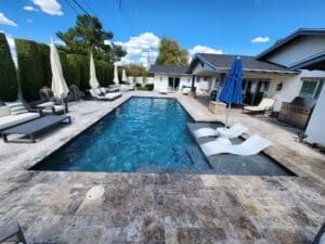 A pool with an umbrella and chairs in the back yard.